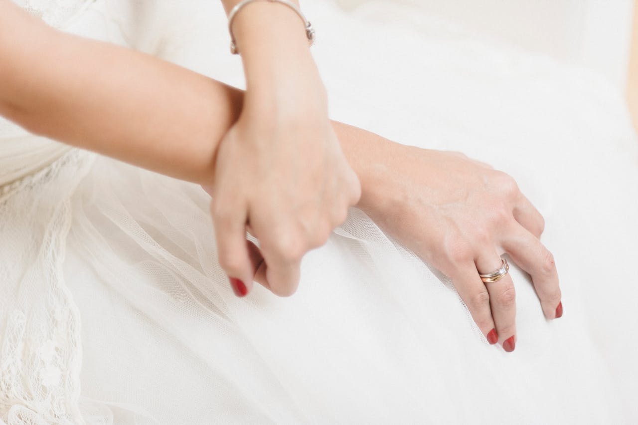 Close-up image showcasing elegant hands with red nails, a wedding ring, and jewelry.
