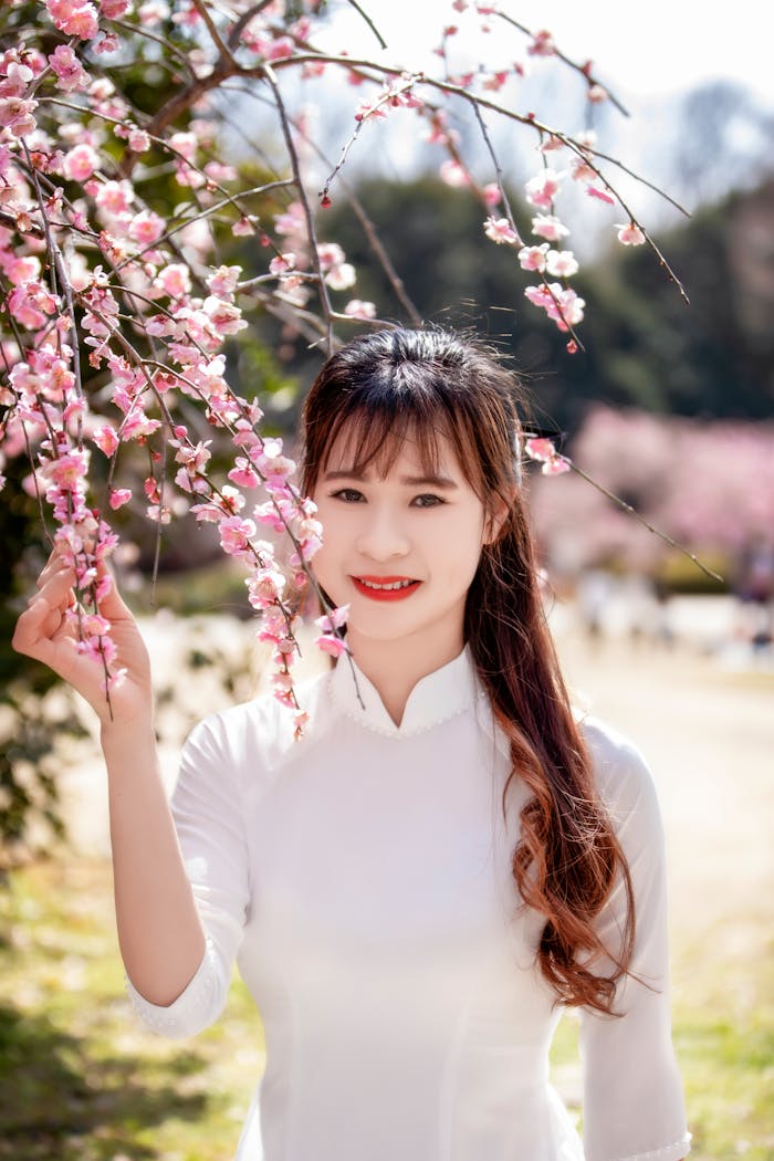 Smiling woman holding cherry blossoms outdoors on a sunny spring day.